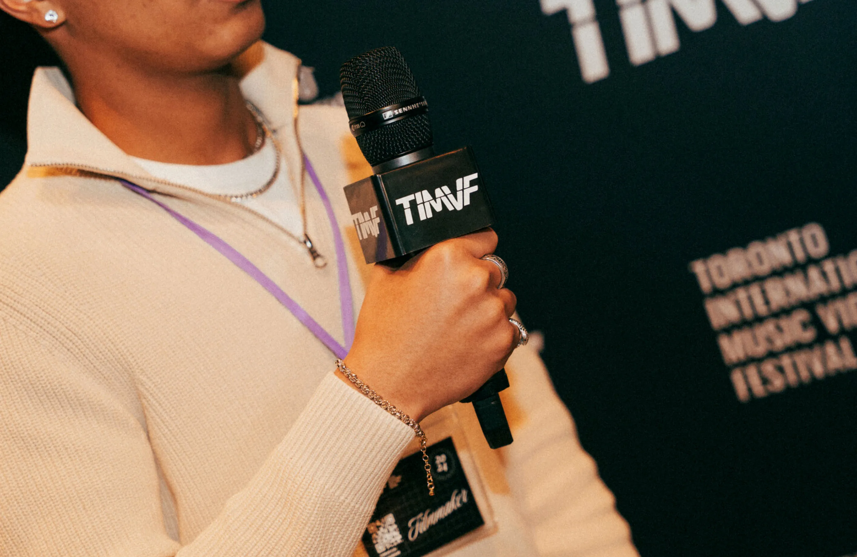 Close-up photo of a man holding a microphone embalzoned with the TIMVF wordmark and wearing a branded lanyard.
